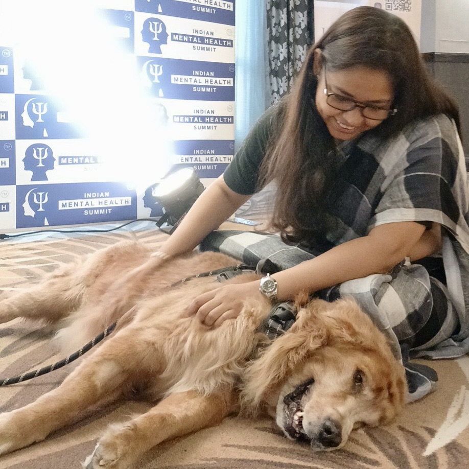 Non-clinical Art Therapist sitting and petting a large, smiling Golden Retriever Therapy Dog at the Indian Mental Health Summit 