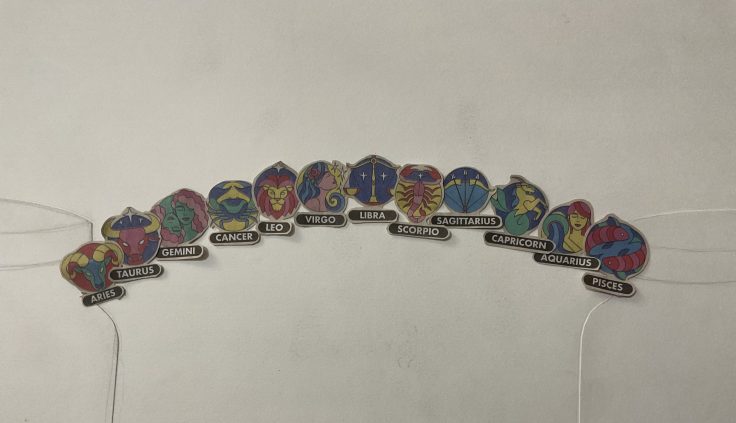 Twelve colorful circular zodiac signs arranged in an arc representing a bridge between two faint jar outlines on white paper